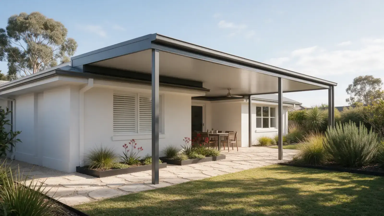 A flat Colorbond patio joined to a white rendered Perth home, with a light grey ceiling, dark grey beams and posts on limestone paving and native garden beds