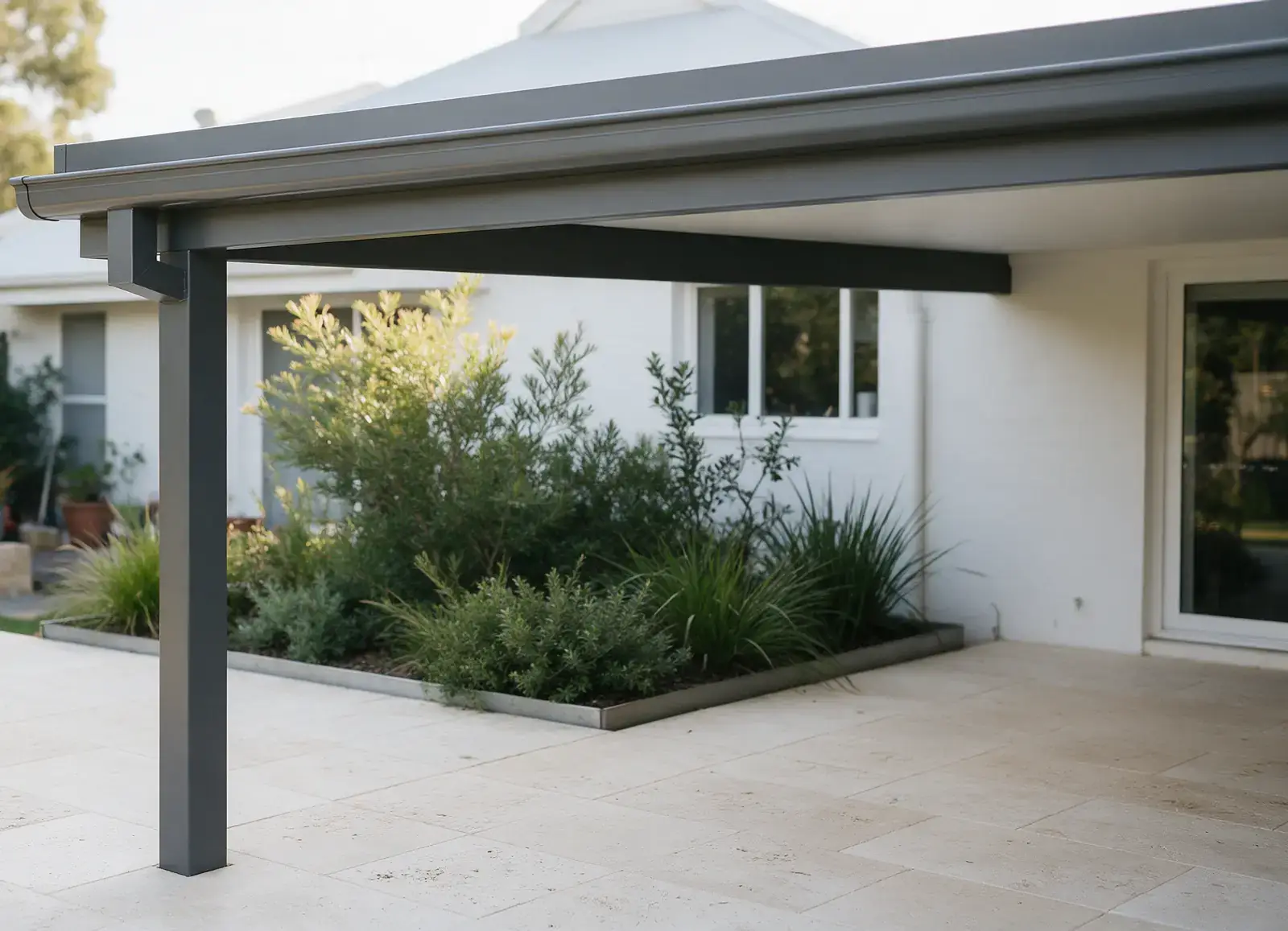 Corner of a flat Colorbond patio in a Perth backyard, with a dark grey post on limestone paving and a steel-edged garden bed set back from it